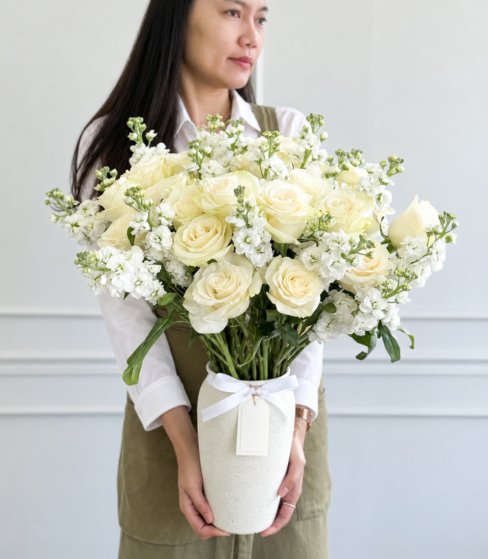 A luxurious vase arrangement of fresh ivory roses and delicate white stock flowers, beautifully