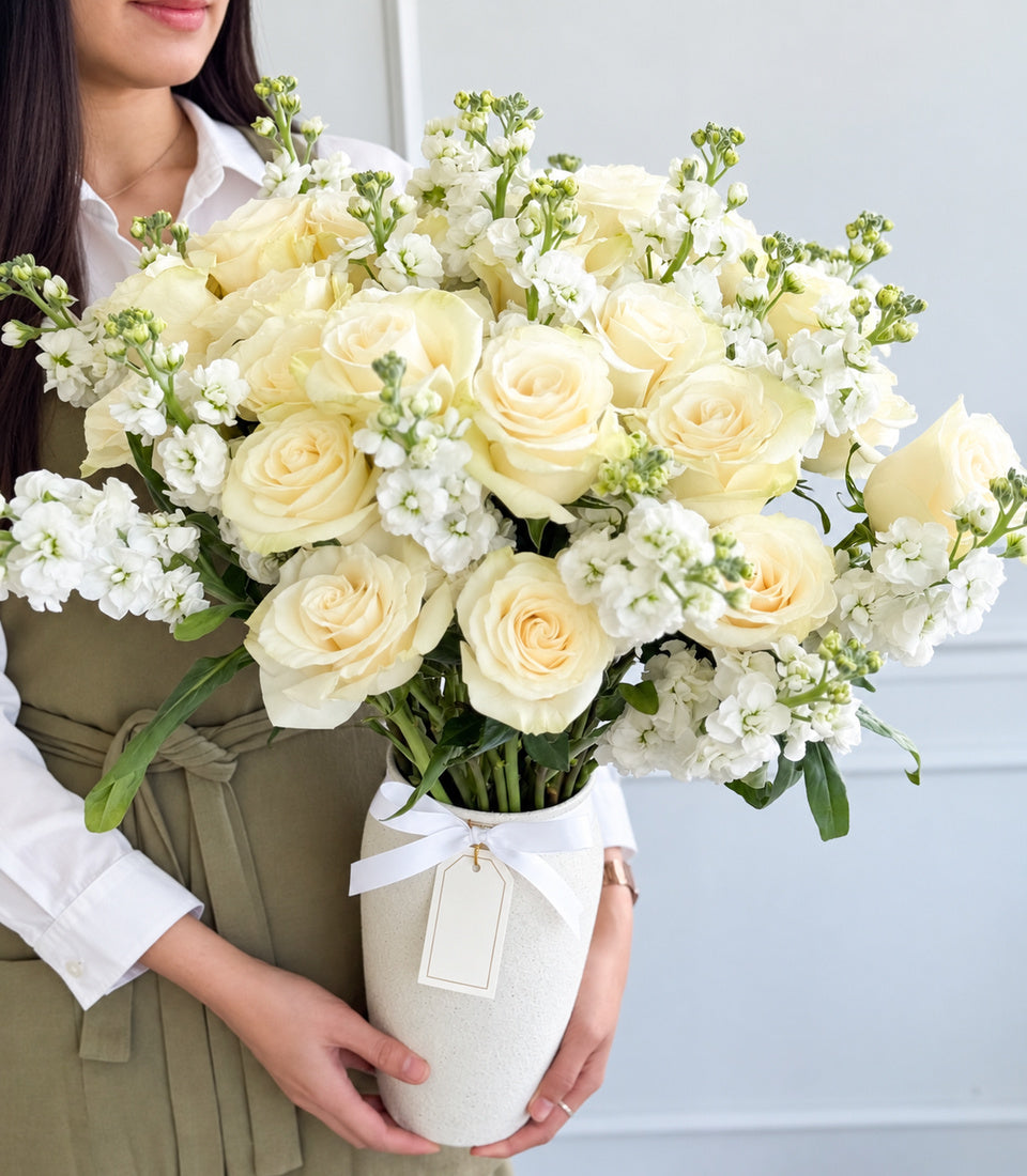 Elegant ivory rose and white stock flower arrangement in a textured vase with a satin ribbon