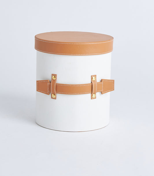 Round white leather gift box with tan lid, gold stud belt closure, and white stitching detail
