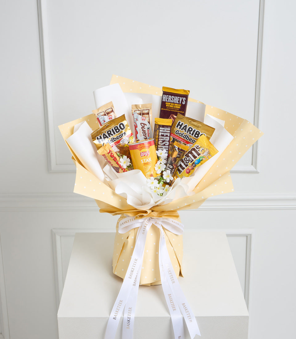 Gold and cream snack bouquet with Haribo, Hershey's, M&Ms, and Lay's chips arranged with white tissue paper and white ribbon bow.